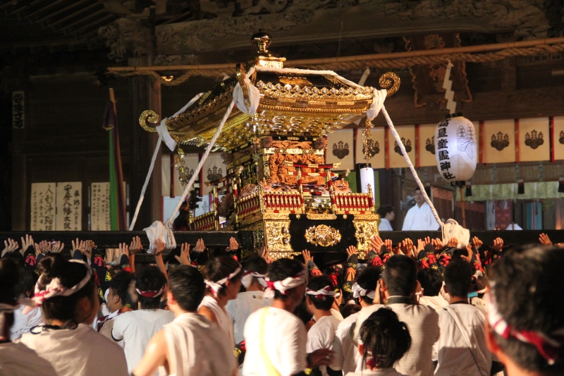 鶴谷八幡宮の社殿前で、白い法被に鉢巻姿の担ぎ手が金色の神輿を頭上に差し上げている夜の様子