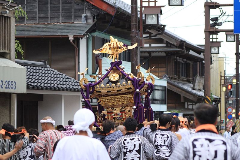 古い商家が並ぶ大多喜の城下町通りを、法被姿の担ぎ手が金色の神輿を担いで進む様子