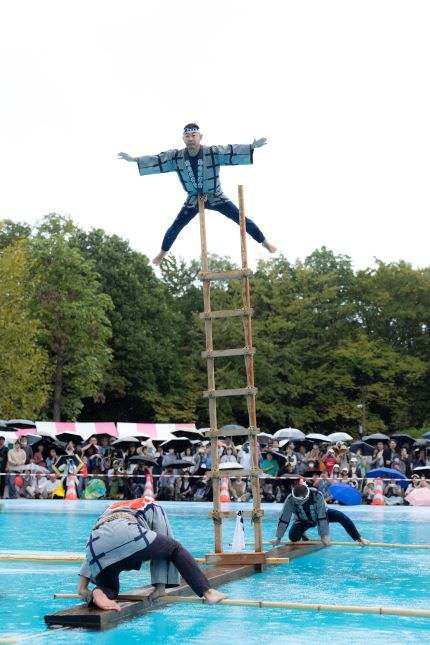 木場公園のイベント池で角材の上に立てたはしごの上で演技する木場の角乗