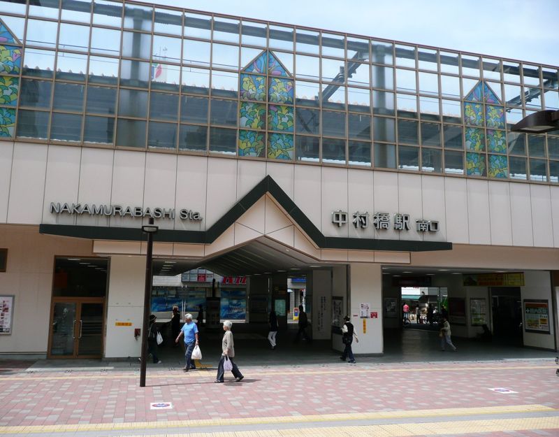 西武池袋線・中村橋駅南口の駅舎。切妻の庇の上にステンドグラス風の色ガラスがはめ込まれ、駅前を買い物客が歩く