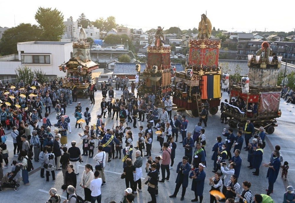 佐倉の秋祭りで、人形を載せた山車と御神酒所が広場に集まり、揃いの半纏を着た町の人たちと見物客が囲んでいる