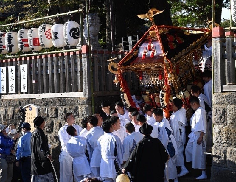 白丁を着た担ぎ手が、神社の石垣の前で麻賀多神社の大神輿を担いでいる