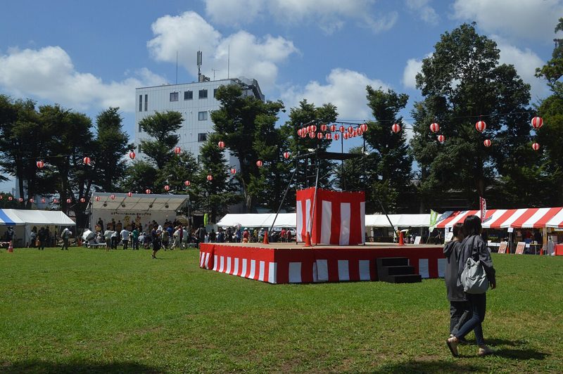 八街市のけやきの森公園。芝生広場に紅白幕のやぐらとテントが並び、周囲をケヤキなどの高木が囲む