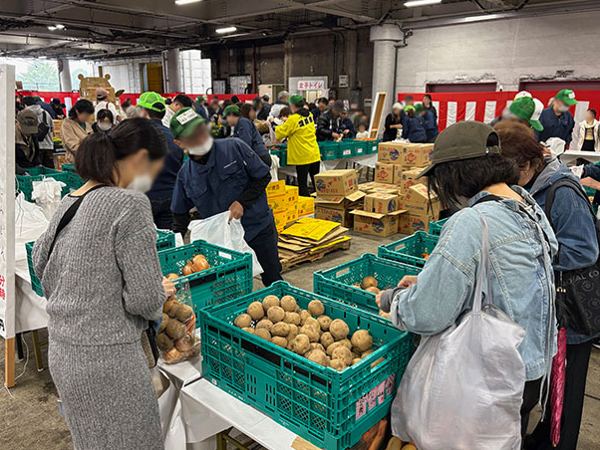 タマネギ詰め放題の看板とじゃがいもを袋に詰める来場者