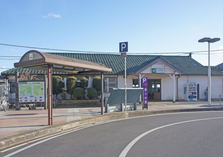 JR総武本線八日市場駅の駅舎。緑の屋根の平屋の駅舎の前に、屋根付きのバス乗り場と駐車場の案内が並ぶ