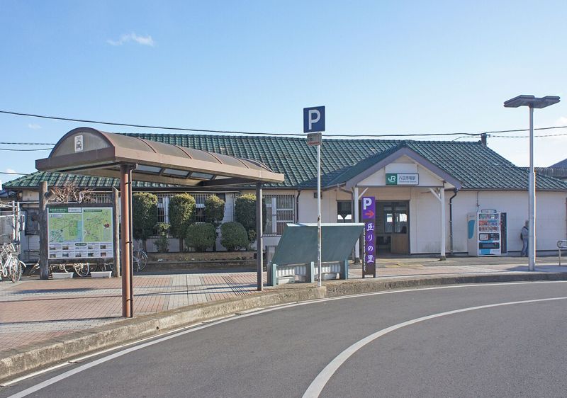 JR総武本線八日市場駅の駅舎。緑の屋根の平屋の駅舎の前に、屋根付きのバス乗り場と駐車場の案内が並ぶ