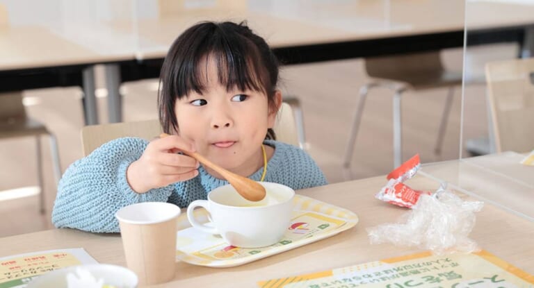 テーブルでカップに入ったスープをスプーンで飲む女の子