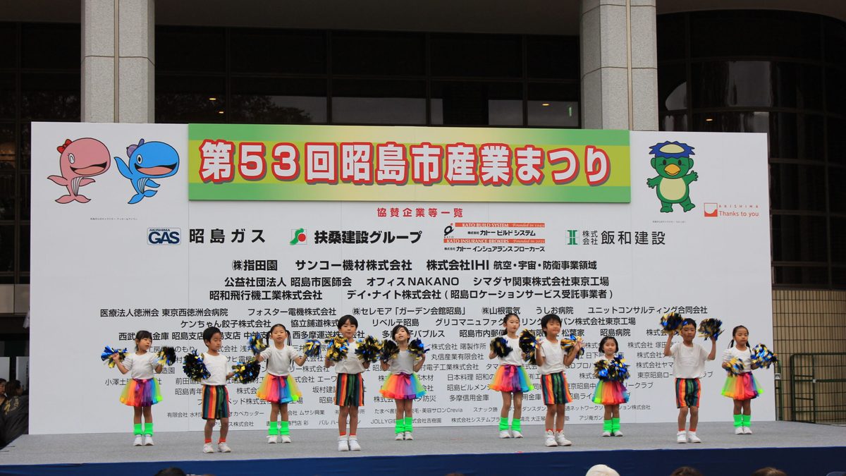 FOSTERホール前の特設ステージで子どもたちがダンスを披露している。背景に「第53回昭島市産業まつり」の看板
