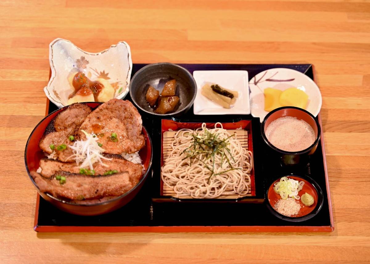 黒い盆に、ねぎをのせた豚丼、ざるそば、つゆ、薬味、小鉢と漬物が並んだ御膳