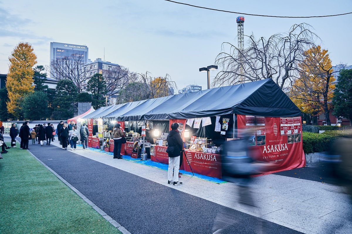 夕暮れの境内に「ASAKUSA」の幕を張った黒いテントが並び、人が買い物をしている