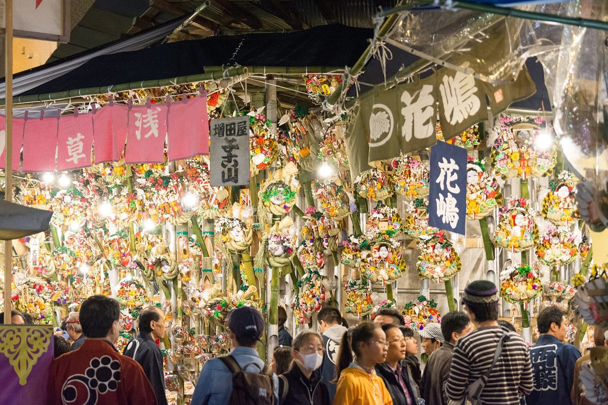 酉の市の境内。熊手がびっしり飾られた店の前を、大勢の参拝客が行き交う