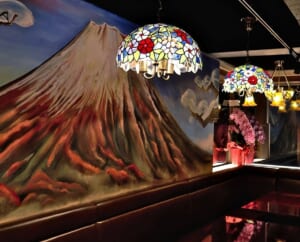 赤い富士山の大きな壁画とステンドグラスのランプがある店内の写真