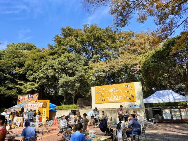 千葉市動物公園の中央広場に並ぶBREW at the ZOOの会場。黄色いステージ看板の前にテーブル席が並び、キッチンカーが出ている