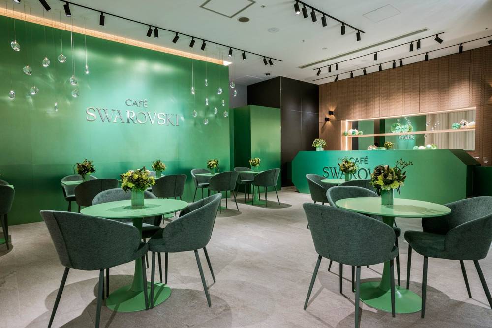 グリーンの壁とテーブル・椅子が並ぶCafé Swarovskiの店内。壁にCAFÉ SWAROVSKIのロゴ
