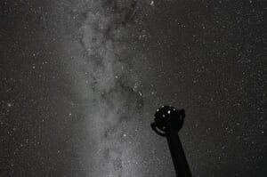 ドームに映し出された天の川と無数の星の下に、球形の恒星投影機のシルエットが立っている
