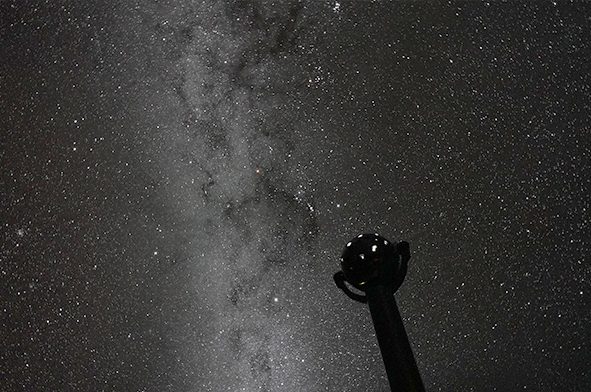 ドームに映し出された天の川と無数の星の下に、球形の恒星投影機のシルエットが立っている
