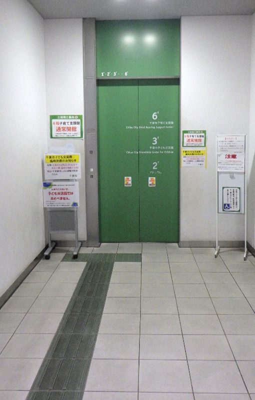 緑色のエレベーターの扉に6階子育て支援館・3階子ども交流館・2階アトリウムの表示。横に「6階子育て支援館 通常開館」「子ども交流館ではあそべません」の掲示