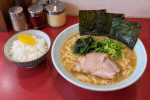 白い丼の豚骨醤油ラーメンに海苔3枚とほうれん草、たくあんをのせたご飯のイメージ画像