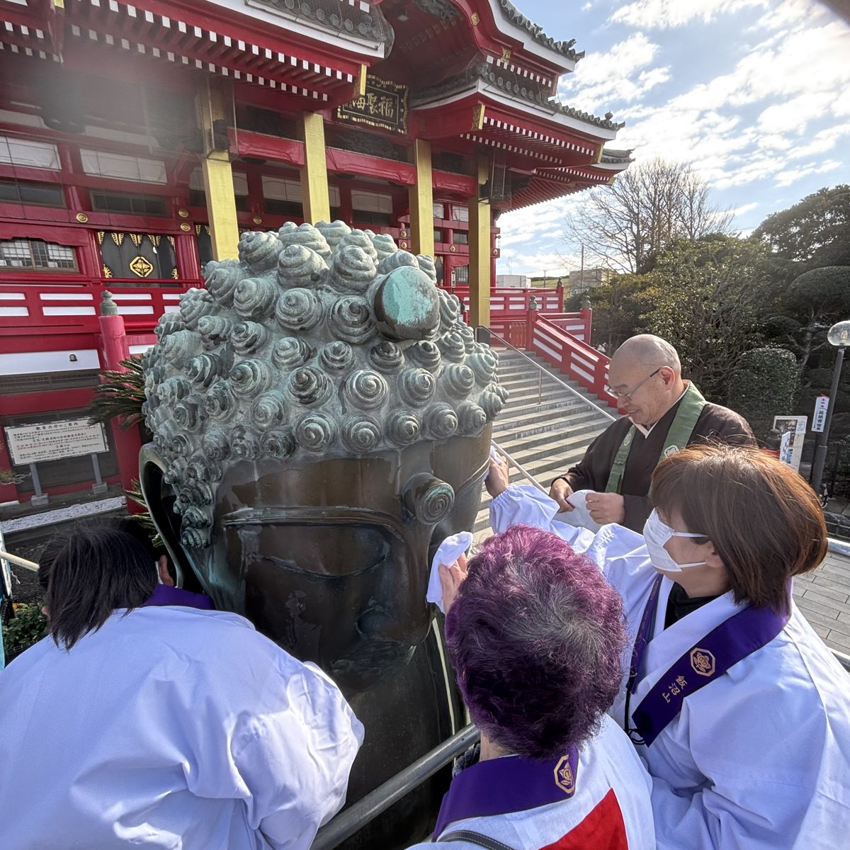 足場の上で白い衣の参加者が大仏の頭を布で拭き、僧侶がそばに立っている