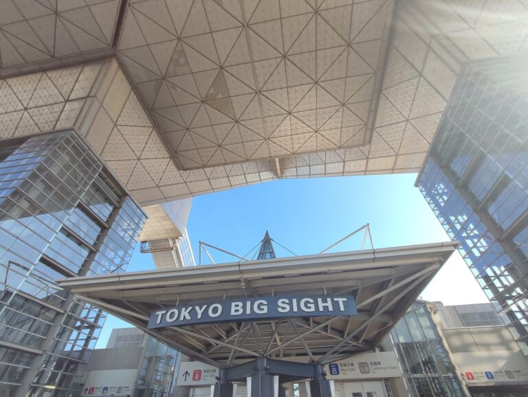 東京ビッグサイトの逆三角形の会議棟を真下の入口付近から見上げた写真。手前に「TOKYO BIG SIGHT」の看板