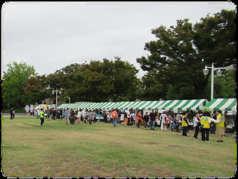 動物愛護フェスタよこはま2025の会場。山下公園の芝生の奥に緑と白のテントの出展ブースが並び、来場者が行き交う
