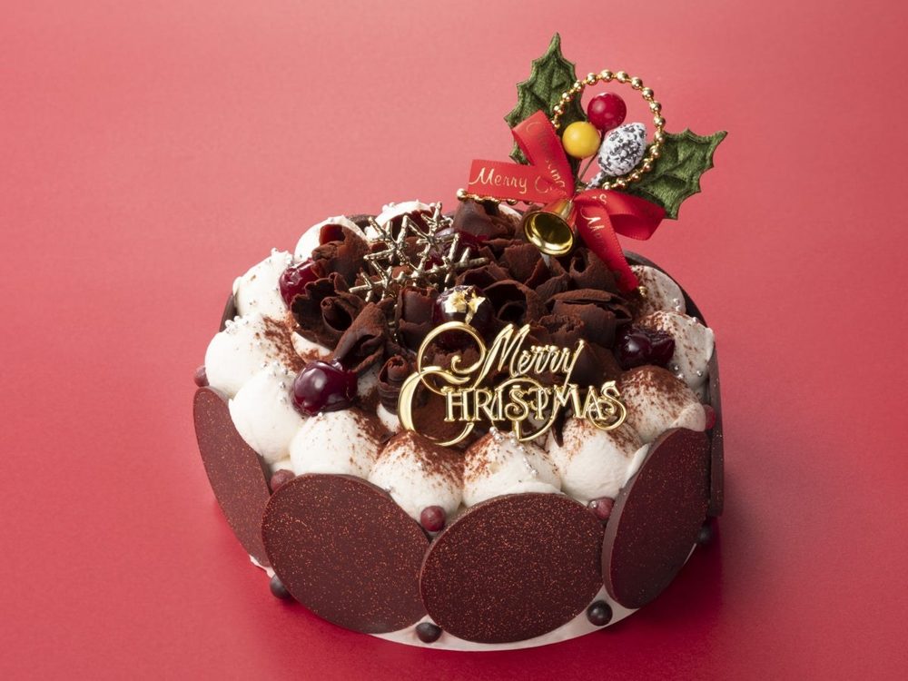チョコレートの円盤を側面に並べ、上にチョコレートの削りとMerry Christmasのプレートを飾った丸いケーキ
