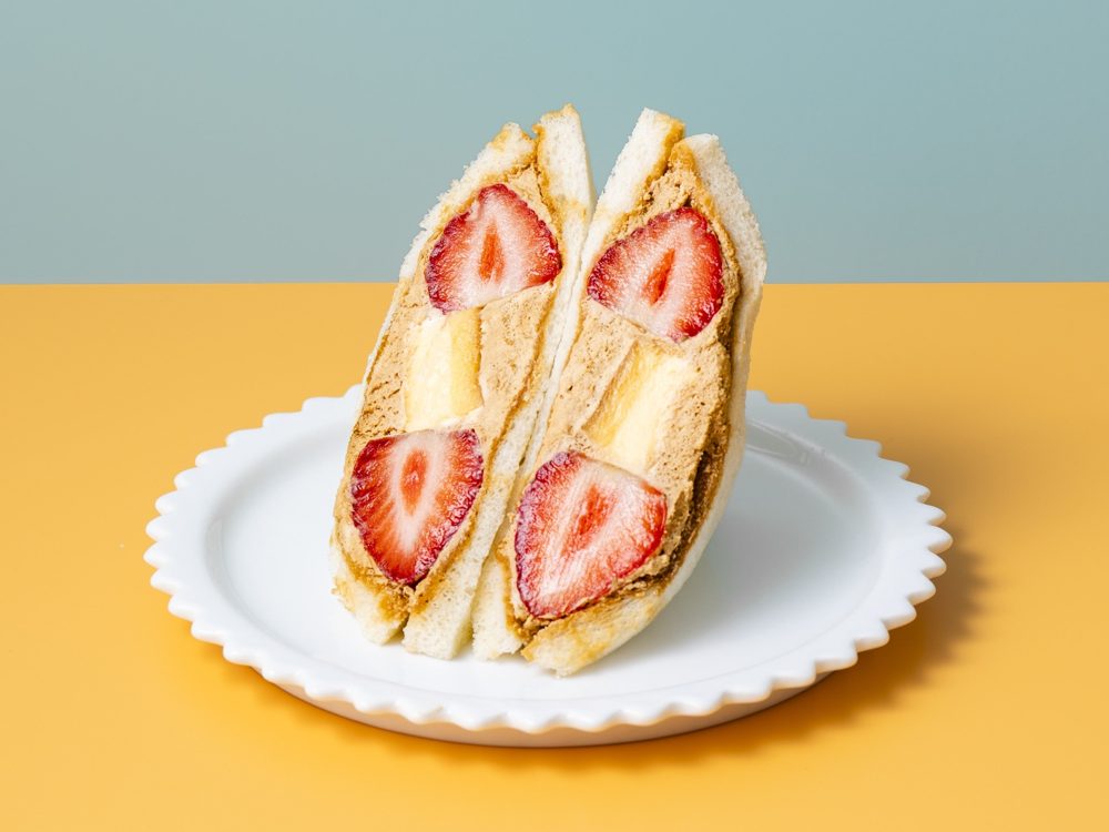 断面に苺とプリン、クリームが見えるサンドイッチを白い皿に立てて並べた写真