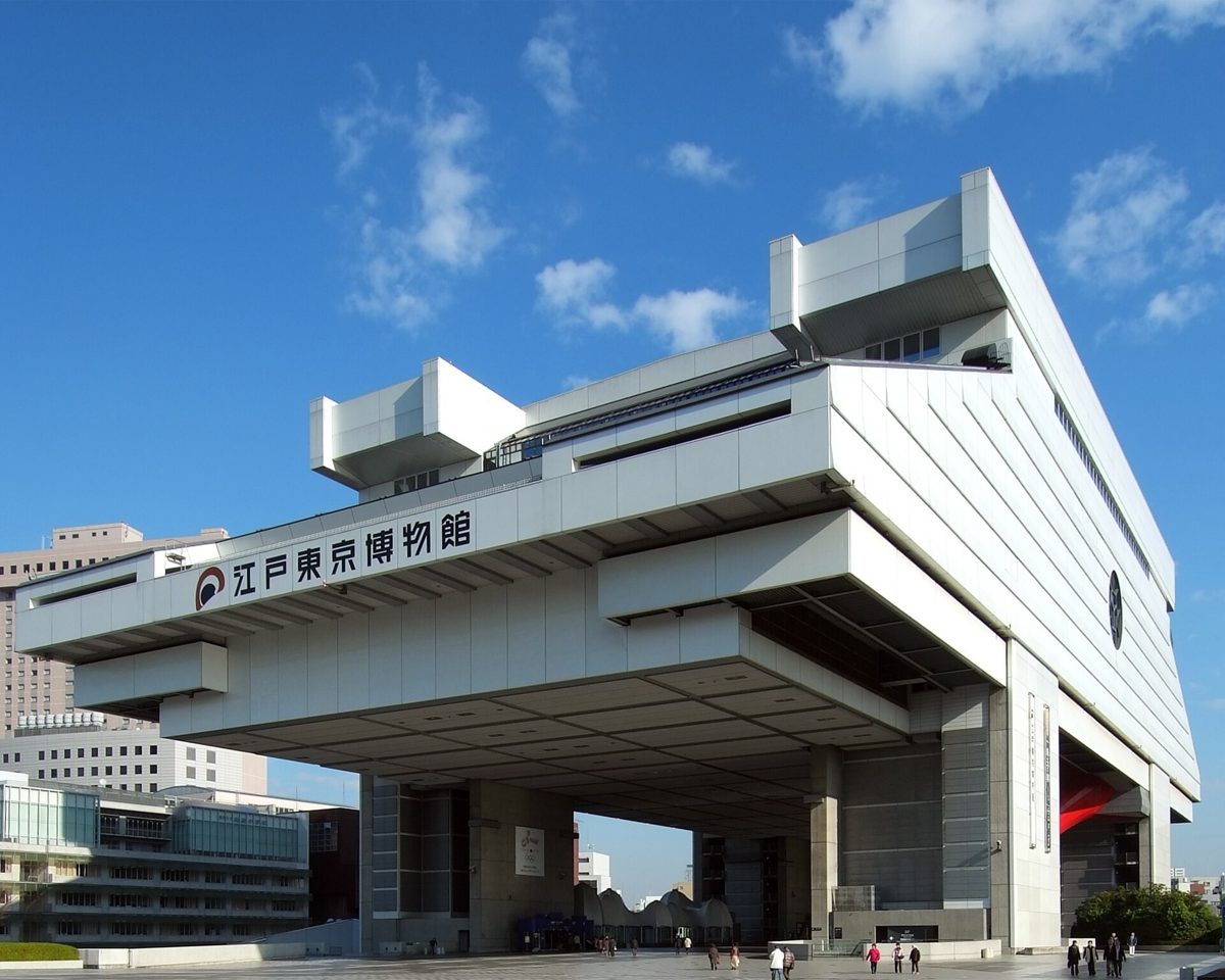 高床式の倉を思わせる白い大きな建物に「江戸東京博物館」の文字。青空の下、手前の広場を人が歩く