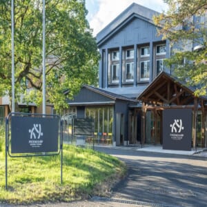 木々に囲まれた濃いグレーの建物と、FRiENDSHiP SAITAMA YOSHIMIのロゴが入った看板が立つ入口