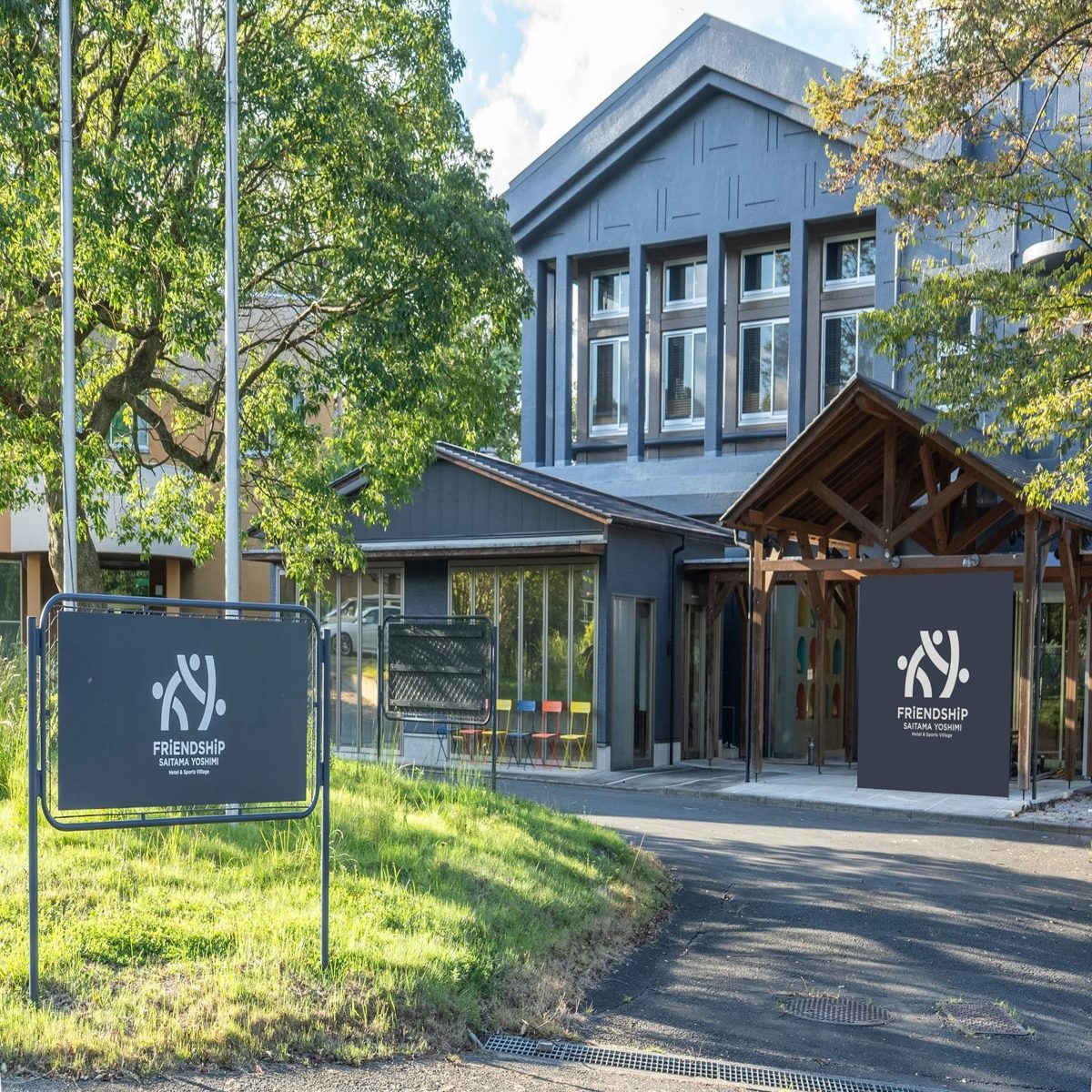 木々に囲まれた濃いグレーの建物と、FRiENDSHiP SAITAMA YOSHIMIのロゴが入った看板が立つ入口