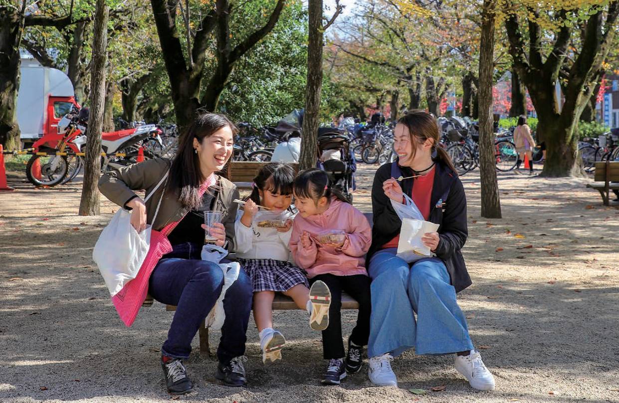 前年の産業まつりで、福岡中央公園の木陰のベンチに座り食べ物を手にする親子連れ