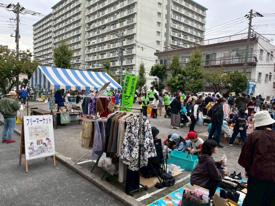 団地の前の広場に洋服や雑貨を並べたフリーマーケットと、テントの下で買い物をする人たち