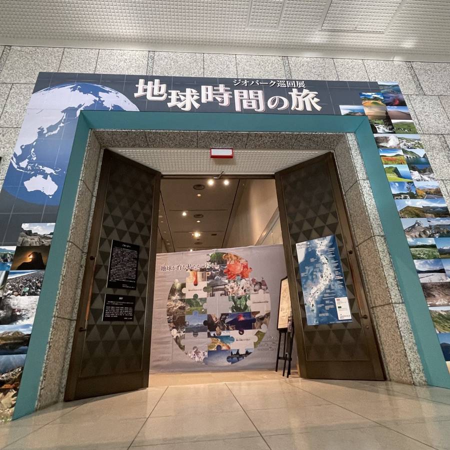 「ジオパーク巡回展 地球時間の旅」の看板と地球の画像、各地の景観写真を貼り並べた展示室の入口ゲート