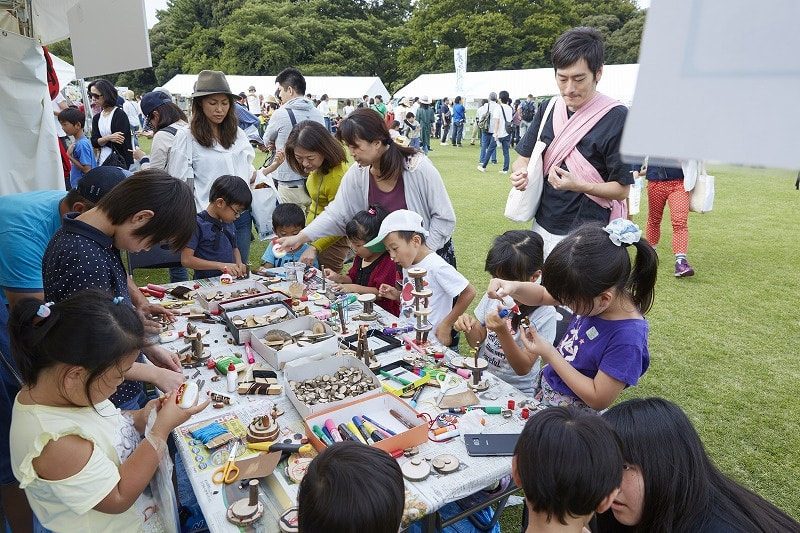 芝生の上のテントで、親子連れが机を囲んで工作をしている様子