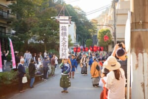 「箱根大名行列」ののぼりを先頭に、時代装束の行列が温泉街の坂道を進む様子。沿道で見物客が撮影している