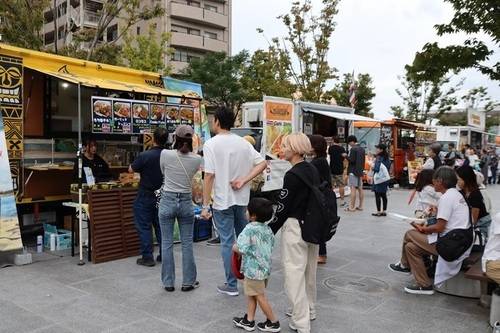 市役所前広場に並ぶキッチンカーと、メニューを見ながら並ぶ来場者