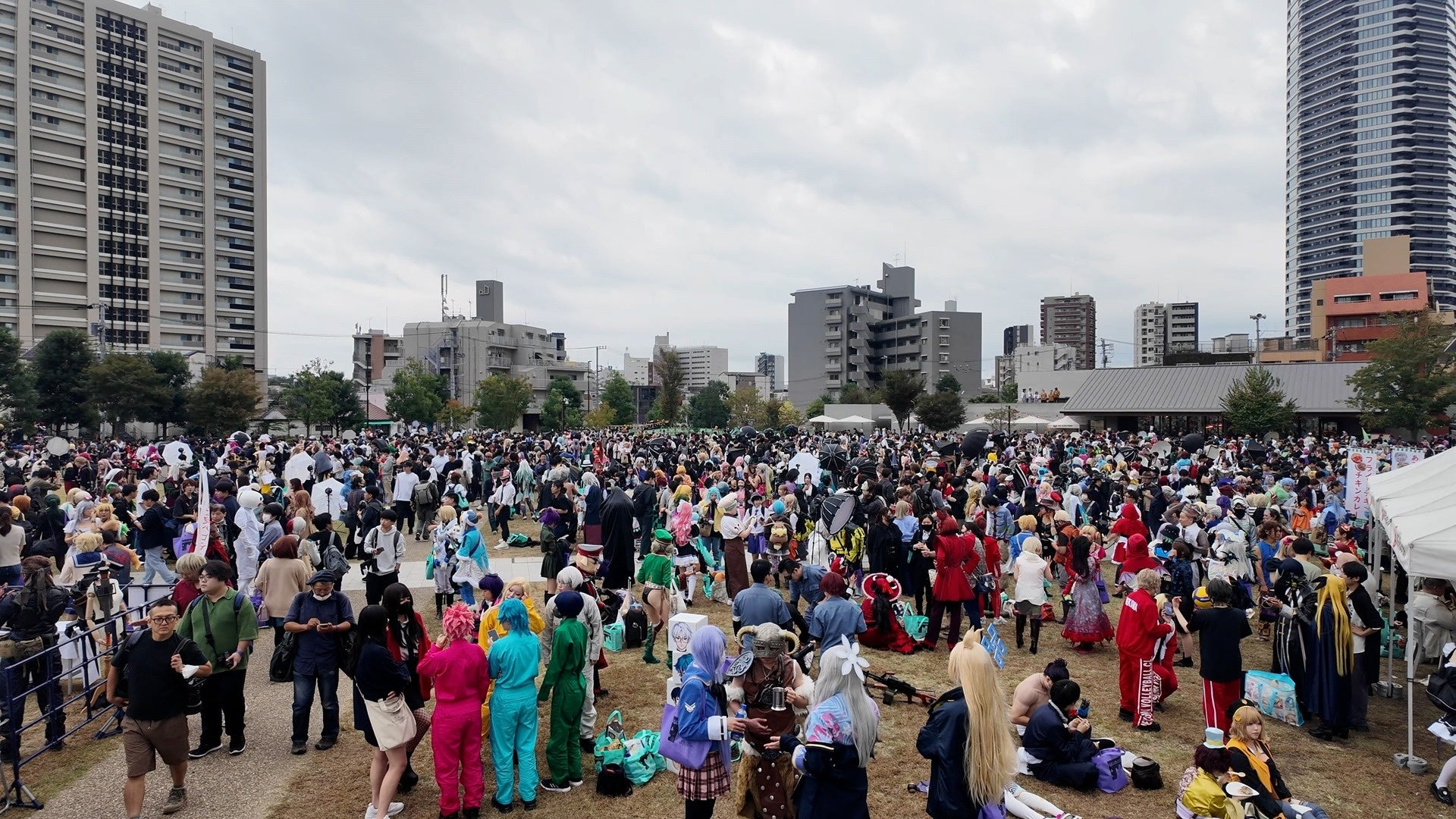2025年の池袋ハロウィンコスプレフェスで、高層ビルを背に公園の芝生広場に大勢のコスプレイヤーと来場者が集まっている様子