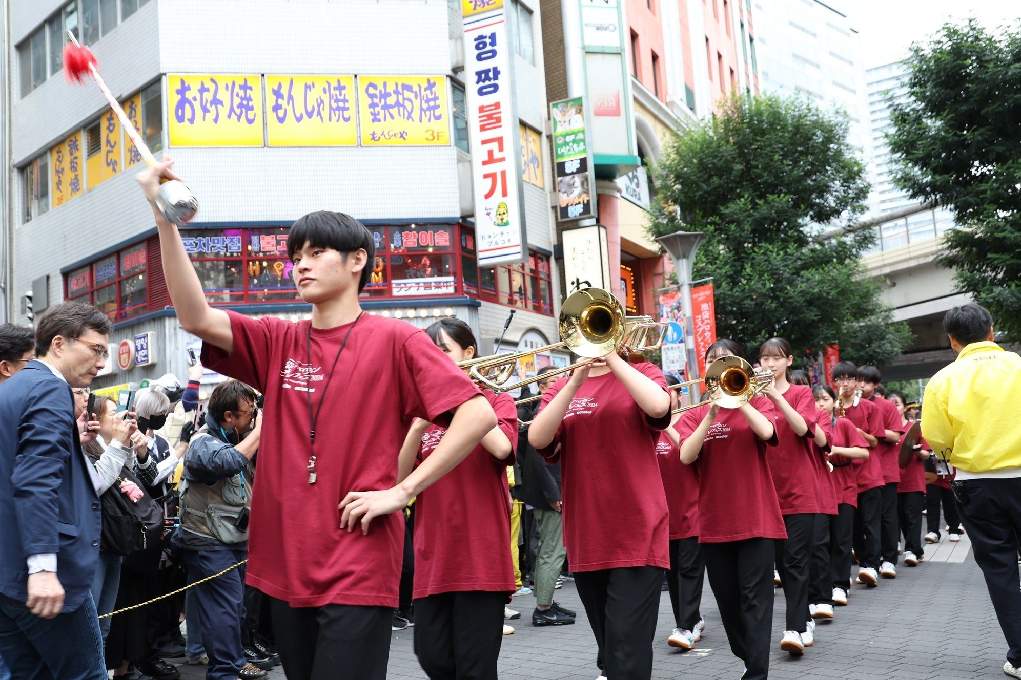 2025年の池ハロのパレードで、赤いTシャツの吹奏楽部が指揮棒を振る先頭に続いて演奏しながら商店街を進む様子