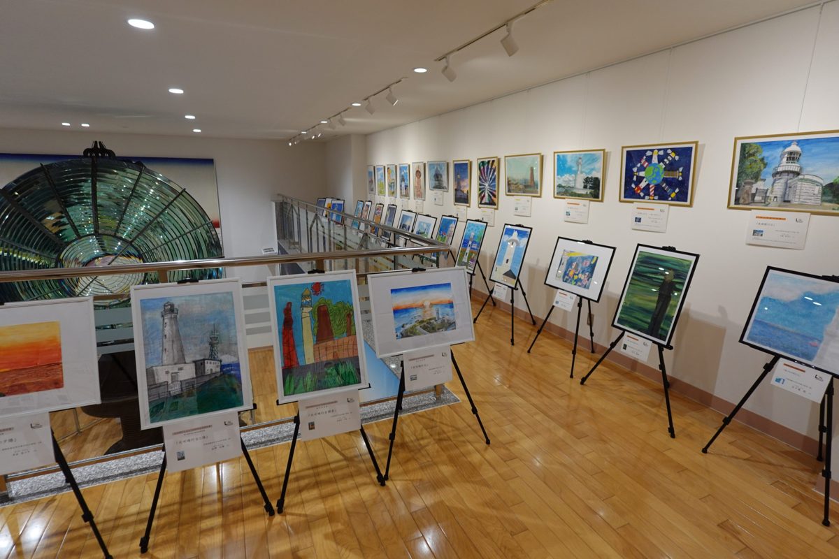 木の床の展示室に大きなレンズと、イーゼルに並んだ灯台の絵