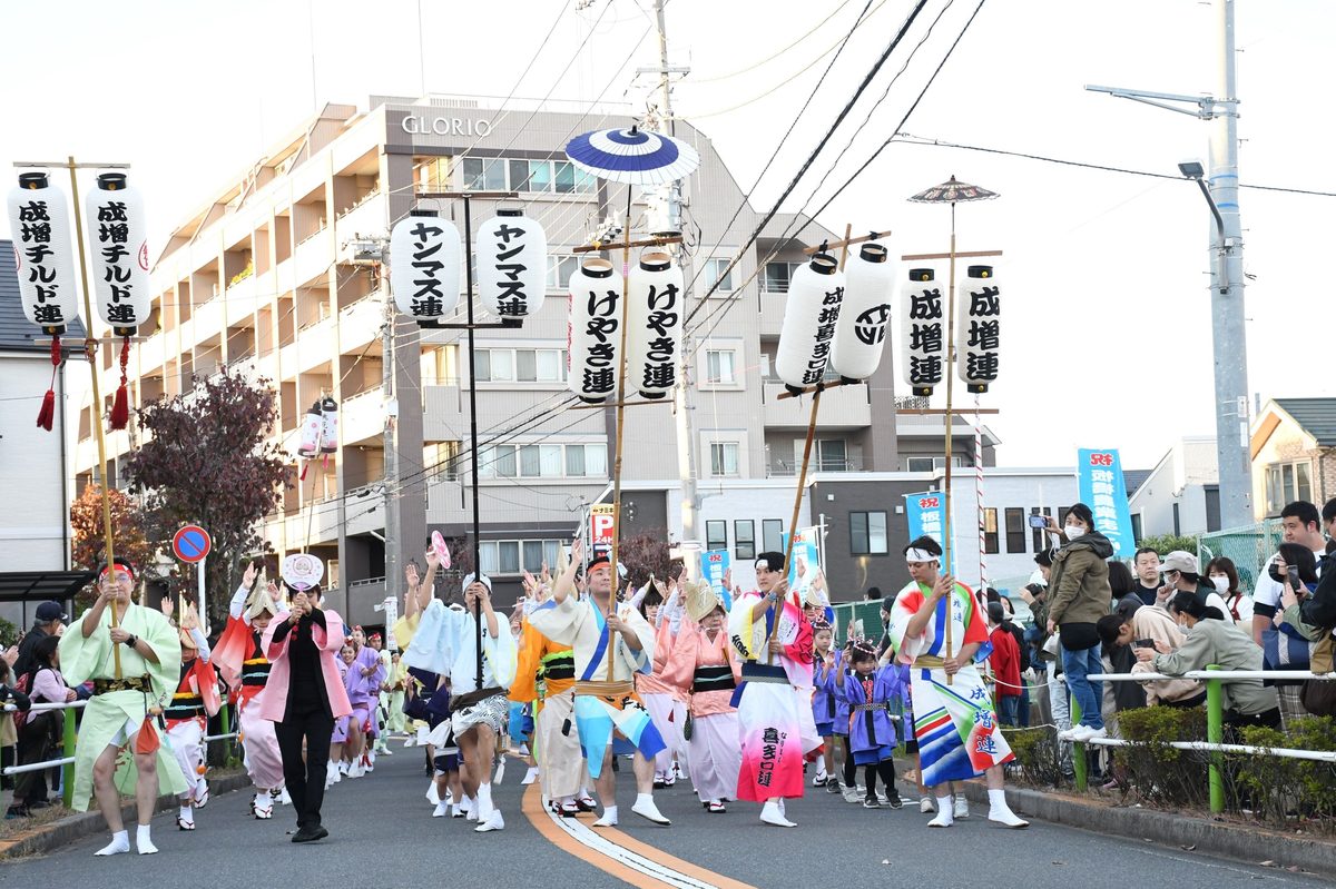 のぼり旗を持ち、色鮮やかな衣装で通りを踊り進むパレードの列と沿道の見物客