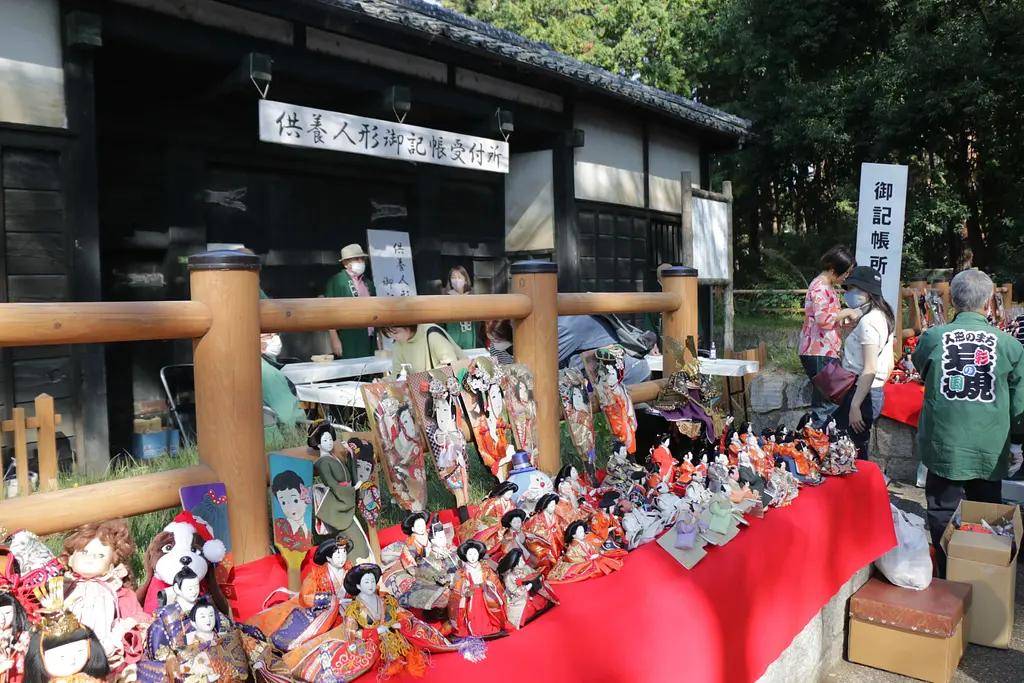 岩槻城址公園の黒門前に並べられた、供養を待つひな人形や羽子板、ぬいぐるみ。奥に「供養人形御記帳受付所」の看板と受付の人たち