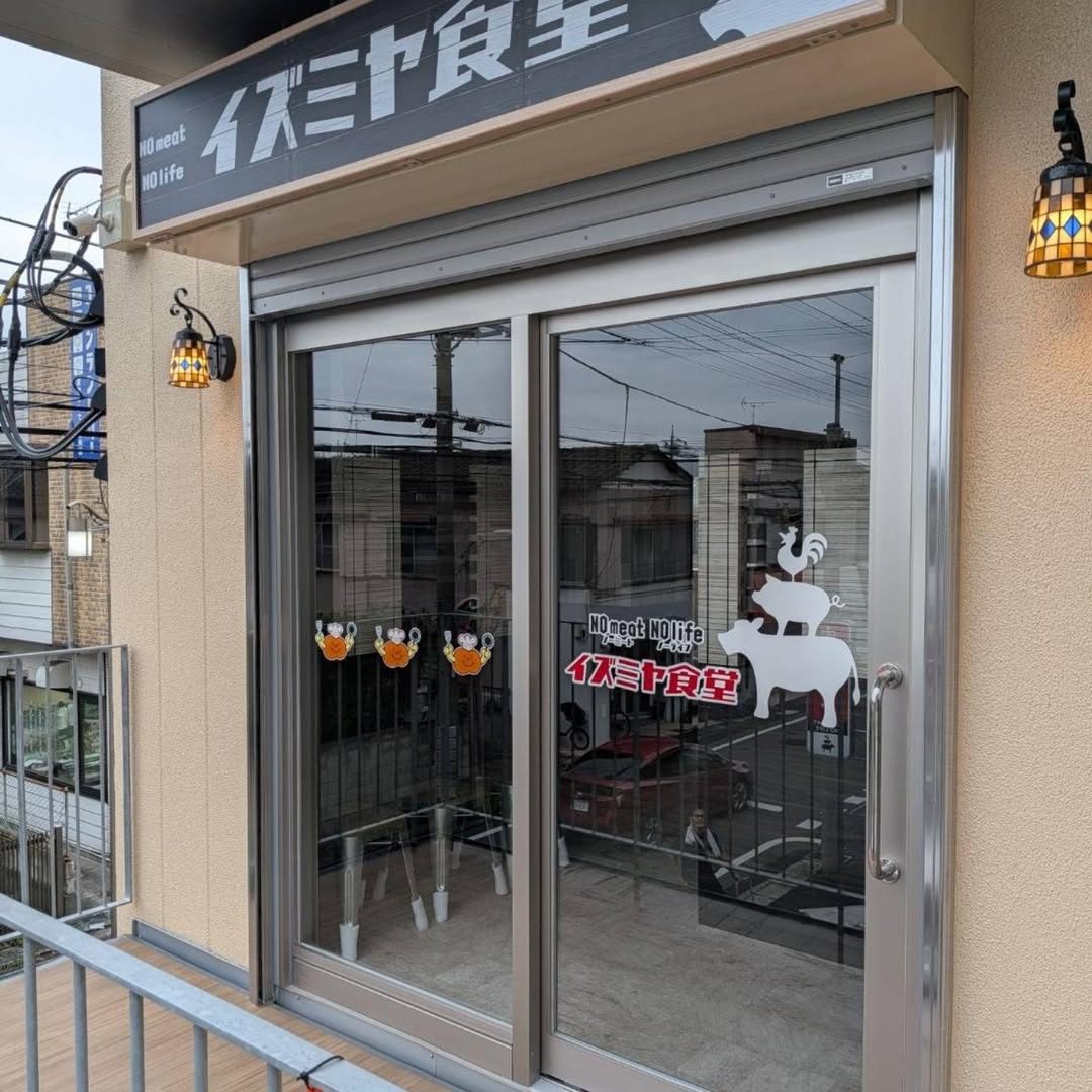 2階の入口の上に「NO meat NO life イズミヤ食堂」の看板。ガラス戸に牛・豚・鶏を重ねた絵と店名が描かれている