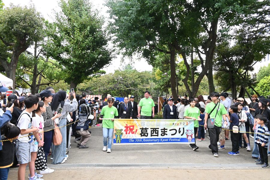 第50回葛西まつりのパレード。祝葛西まつりの横断幕を持った先頭を、沿道の親子が見送っている