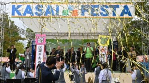 第50回葛西まつりの開会式。KASAI FESTAと書かれたステージで金色のテープが舞い、手前で吹奏楽部が演奏している