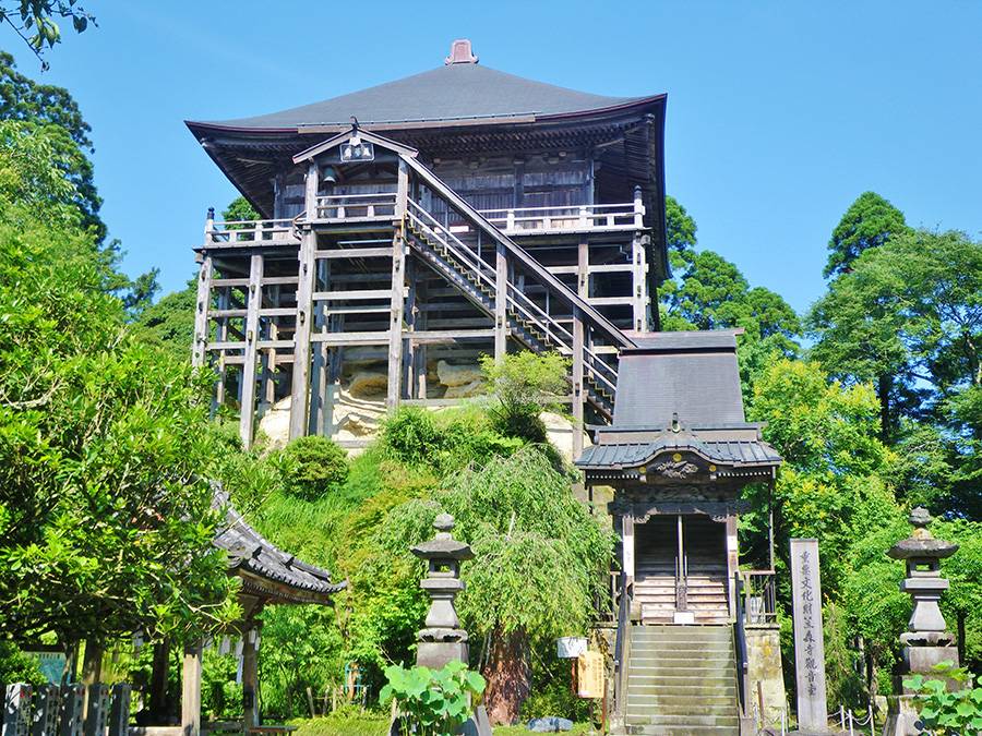 緑の木々に囲まれた岩の上に、何本もの柱で支えられて建つ笠森観音の観音堂と、手前の石段と山門
