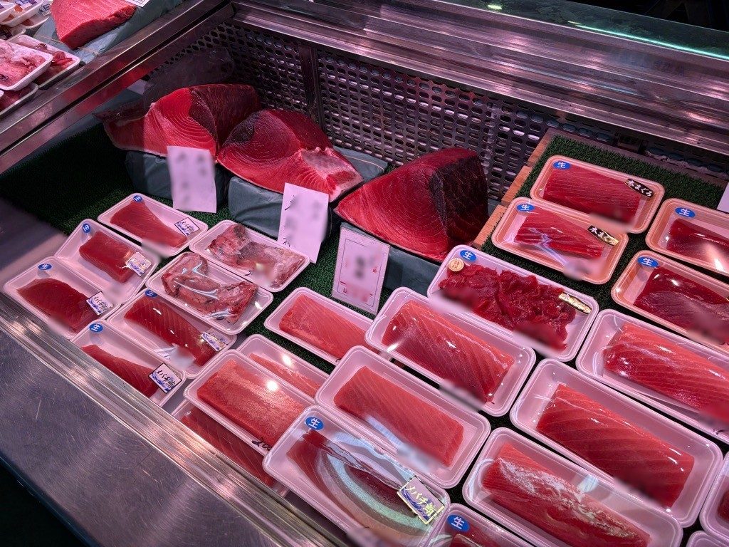 ショーケースに並ぶパック詰めのまぐろの赤身と、奥に置かれたまぐろの塊