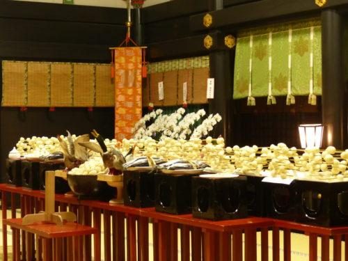 赤い欄干の奥の黒い台に、白い団子がたくさん積まれ、鳥や魚の神饌と白い胡蝶蘭が並んでいる