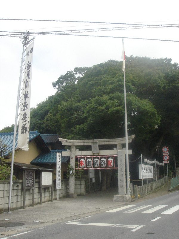 道路に面した検見川神社の石の鳥居。奉祝の提灯が掛かり、奥の森の上に社殿がある