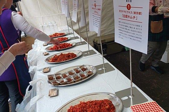 試食台に出品番号の札と説明パネルを立てたキムチの皿が並ぶ。手前の札は「第8回 1 タカヤマピクルス（東京都）白菜キムチ」