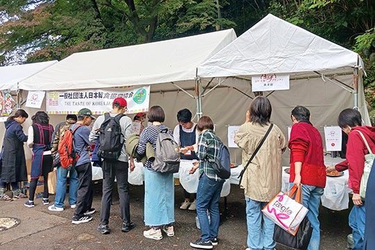 第8回全国キムチグランプリの会場。白いテントの前に来場者が並び、日本韓食振興協会の横断幕が掛かった試食テーブルでキムチを受け取っている
